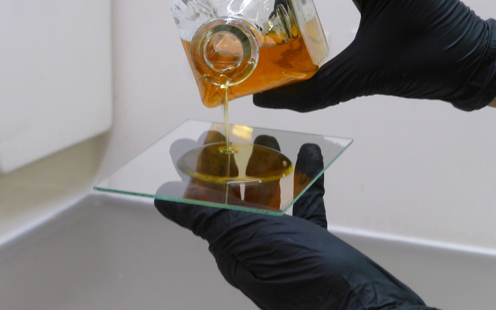 Gloved hands pour amber liquid collodion onto a glass plate