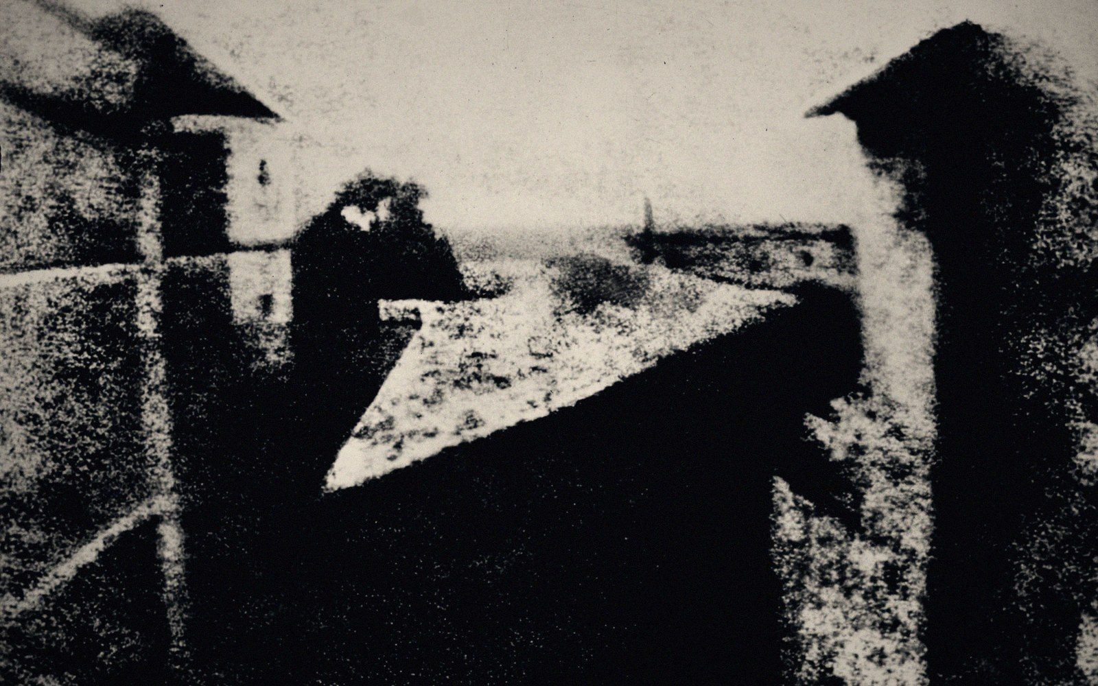 Grainy early photograph showing rooftops and buildings viewed from a window