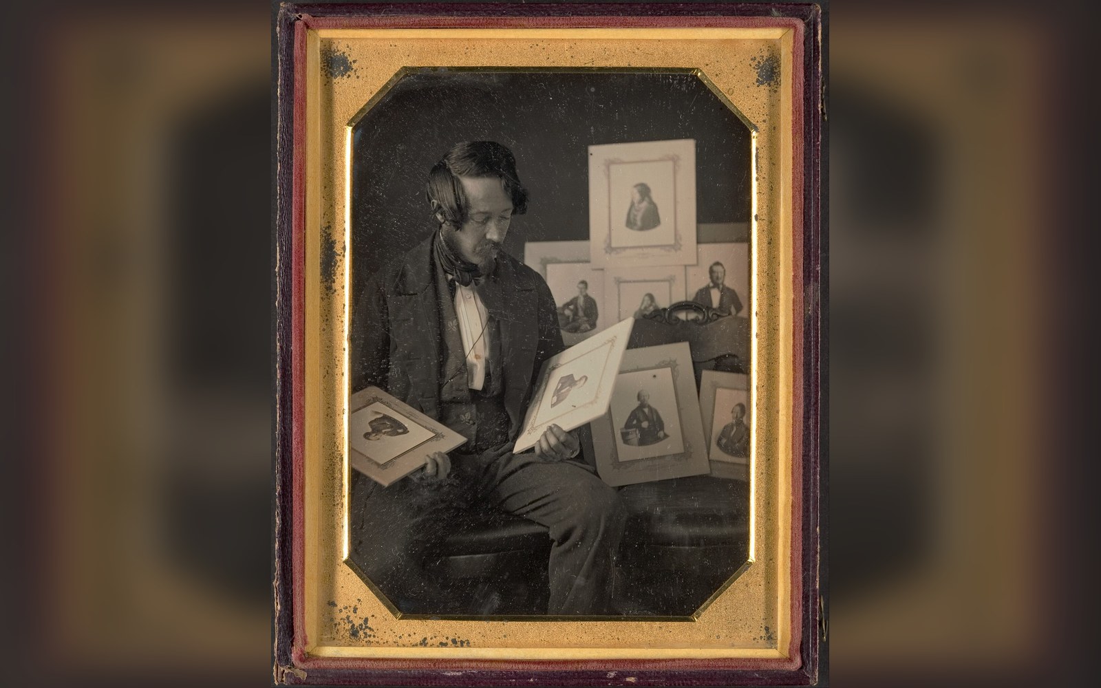 Antique daguerreotype portrait of a seated man examining framed portrait photographs in his lap